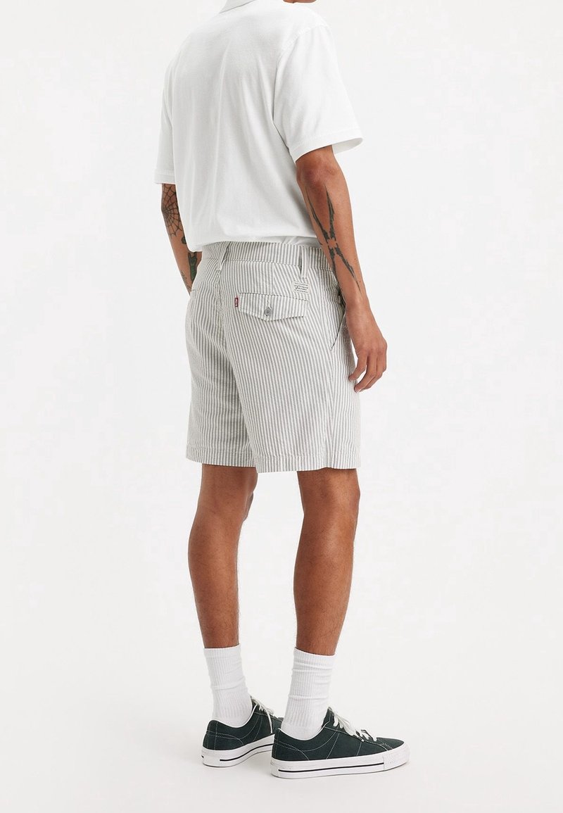 Shorts rayés en gris clair et blanc, confectionnés dans un tissu à finition texturée. Dotés d'une poche arrière et d'une coupe décontractée. Portés avec des baskets foncées.