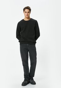 Sudadera negra de cuello redondo, jeans oscuros y zapatillas negras. Diseño simple, forma ajustada, textura de algodón, sin patrones ni herrajes visibles.