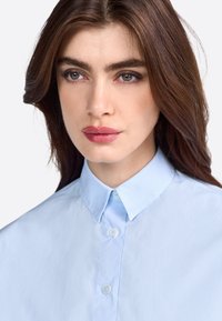 Light blue collared shirt with a button front and smooth texture, featuring a classic design and subtle sheen.