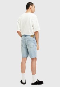 Ljusblå denimshorts med fem fickor, en brun läderlapp och en lös passform. Matchas med en vit t-shirt och svarta skor.