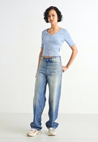 Svijetloplavi rebrasti crop top s kratkim rukavima i detaljima od dugmadi, u kombinaciji s trapericama viskog struka svijetlosive boje. Neutralni tenisice.
