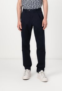 Marineblauwe broek met een rechte pasvorm, voorzien van een knoopsluiting en zakken. Gedirigeerd met witte sneakers en een geblokt shirt.