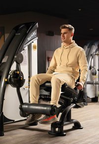 Macchina per esercizi con una struttura nera elegante, sedile regolabile e rulli imbottiti neri. Utente in felpa e pantaloni beige chiaro afferra le maniglie.