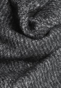 Gros plan d'un tissu en laine gris foncé avec une texture douce et duveteuse et des fibres tissées ainsi que des plis visibles.