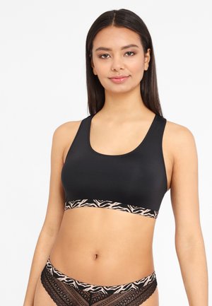 Schwarzer BH aus glattem Stoff mit einem breiten, gemusterten Bund mit rosa Zebramuster, getragen von einem Modell vor einem schlichten weißen Hintergrund.