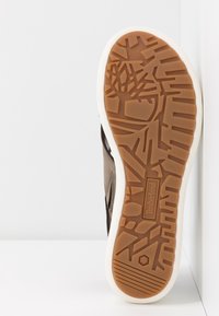 Semelle d'une chaussure Timberland marron avec motif de bande de roulement texturé et semelle intermédiaire blanche, photographiée sur un fond blanc.