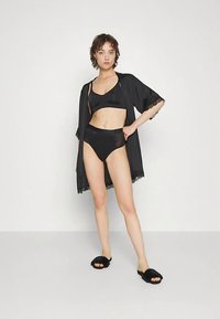Conjunto de sujetador de satén negro y braguita de talle alto, combinado con un kimono negro transparente con ribete de encaje, acompañado de sandalias negras peludas tipo slide.