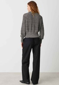 Maglione grigio a maglia con una finitura testurizzata, orlo a coste e spalle scese, abbinato a pantaloni neri a gamba larga e scarpe nere.