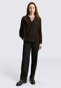 Brown patterned blouse with a drawstring neckline, long sleeves, paired with black wide-leg trousers and black shoes. Smooth texture.