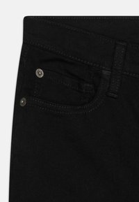 Jeans de mezclilla negros con un diseño clásico, que cuentan con un bolsillo frontal y detalles en metal. Textura suave con sutiles acentos de costura.