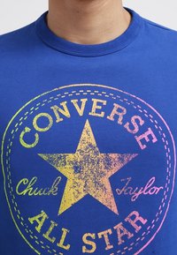 T-shirt en coton bleu avec un grand motif multicolore d'une étoile et un texte indiquant "CONVERSE Chuck Taylor ALL STAR".