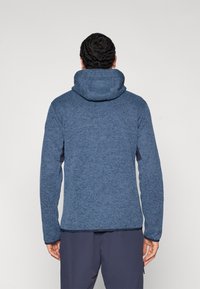 Μπλε υφασμάτινο μπουφάν από φλις με κουκούλα, μακριά μανίκια και εφαρμοστή σχεδίαση. Διαθέτει χαρακτηριστικό ψαροκόκκαλο μοτίβο στο ύφασμα.