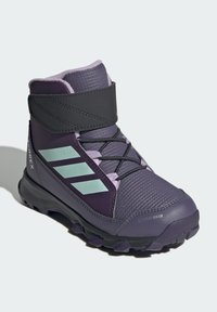 Purple hiking boot with a textured surface, black strap, and light blue accents. Features a rugged sole for traction and insulation details.