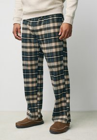 Rutiga loungebyxor av mjukt tyg, med mörkgrön, bejg och brun färg. Löst sittande med resårmidja.