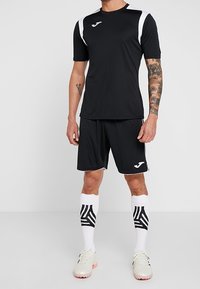 Musta urheiluversio valkoisilla yksityiskohdilla, siihen sopivat shortsit ja polven yli ulottuvat sukat, joissa on musta-valkoisia kuvioita. Kevyt, urheilullinen muotoilu.