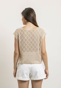 Haut en tricot beige avec un motif en losange et des manches courtes, associé à un short blanc retroussé. Le tissu semble léger et texturé.