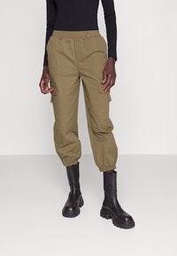 Khaki cargo kalhoty s elastickým pasem a manžetami na kotnících, s postranními kapsami. V kombinaci s černými botami do půli lýtek.