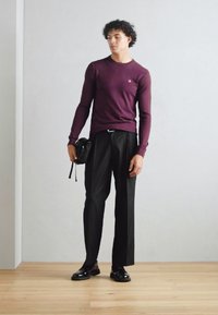 Maglione a maniche lunghe bordeaux abbinato a pantaloni neri su misura e scarpe nere. Tiene una piccola borsa nera. Design minimalista, linee pulite.