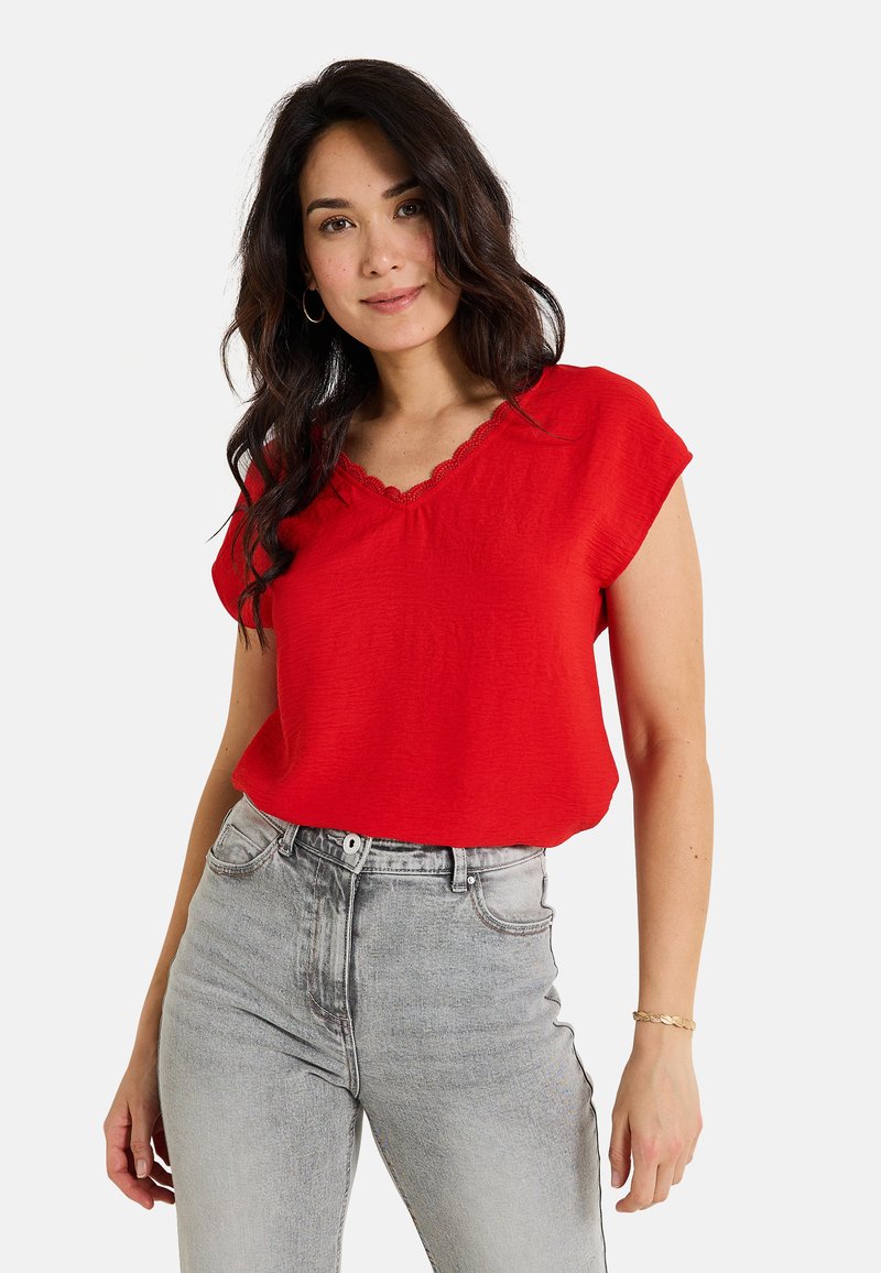 Haut rouge à manches courtes avec un décolleté en V à bordure festonnée, en tissu léger, associé à un jean gris délavé taille haute.