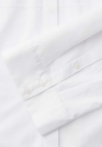 Ärmel eines weißen Hemd mit geknöpftem Manschettenabschluss, flach auf dem passenden weißen Stoffhintergrund ausgelegt.