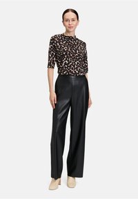 Czarne spodnie z szerokimi nogawkami wykonane z materiału skóropodobnego, z wysokim stanem, w połączeniu z bluzką z krótkim rękawem w brązowy i kremowy abstrakcyjny wzór.