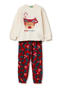 Sudadera crema con un gráfico de chocolate caliente y pantalones de pijama rojos con un patrón de acebo y bayas sobre un fondo rojo oscuro.