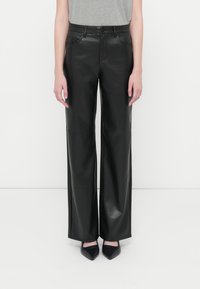 Fekete műbőr trapéznadrág elülső zsebekkel és sima textúrával, fekete hegyes sarkúcipőkkel és szürke toppal kombinálva.