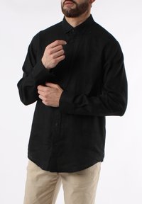 Camicetta nera a maniche lunghe realizzata in tessuto leggero, con chiusura a bottoni, colletto appuntito e vestibilità comoda. Presenta un orlo curvo.