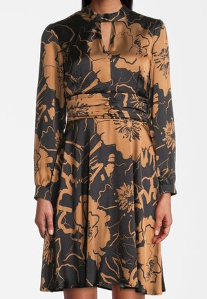 Vrouw draagt een lange mouw zwarte en beige bloemenjurk met een hoge halslijn, keyhole-uitgesneden detail en gerimpelde taille.