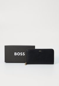 Portafoglio in pelle nera con design zip-around, dotato di hardware dorato e logo "BOSS" impresso. Include una scatola branded nera.