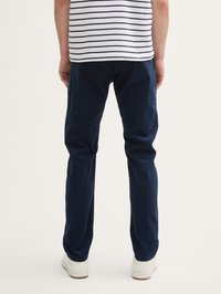 Pantalon en coton bleu marine à coupe droite, présentant une texture lisse et un design ajusté, associé à des baskets blanches.