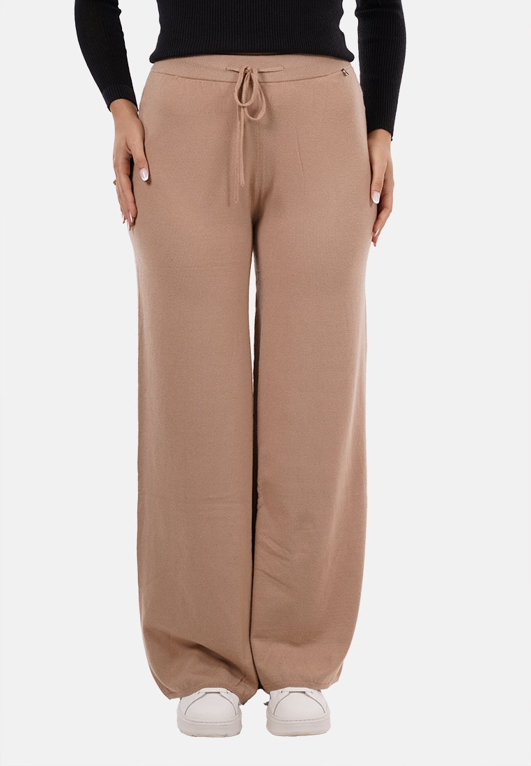 Pantaloni beige a gamba larga con vita elastica e coulisse, caratterizzati da una texture liscia e una vestibilità rilassata, abbinati a sneakers bianche.