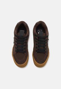 Baskets en suède marron avec lacets noirs et semelles en caoutchouc. Elles présentent une couture contrastante et une petite étiquette de logo sur le côté.