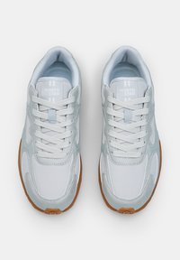 Baskets de sport gris clair avec empiècements en maille et synthétiques, présentant un logo blanc, des lacets ronds et une semelle en caoutchouc gomme avec un profil de semelle prononcé.