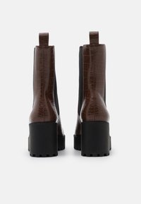 Botas de tobillo marrones con patrón de cocodrilo, con un tacón grueso negro y laterales elásticos, con bucles en la parte trasera para facilitar su puesta.