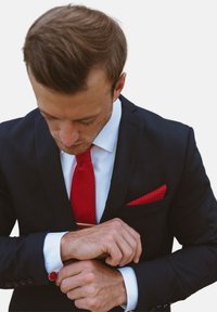 Completo nero con camicia bianca, cravatta rossa a trama e fazzoletto da taschino rosso abbinato. I gemelli sono rotondi con un design rosso.