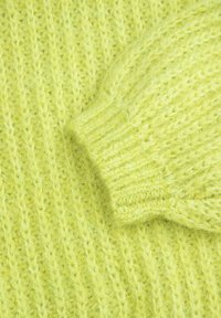 Jasnozielony sweter dzianinowy z teksturowanym wzorem, ściągaczami i miękką, puszystą włóczką. Zbliżenie podkreśla materiał i wzór.