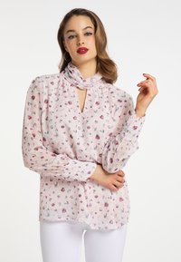 Bluse med blomsterprint i lyserødt stof med en blød, gennemsigtig tekstur. Har en høj hals med nøglehul-design og lange, puffede ærmer.
