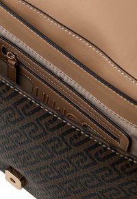 Interior de bolso de cuero marrón con compartimentos color canela y forro a rayas. Incluye un bolsillo con cremallera y un detalle de herrajes dorados.