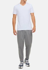 Hvid kortærmet V-hals T-shirt parret med grå tapered bukser og hvid/navy athletic sko. Simpelt design og afslappet pasform.