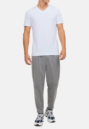 T-shirt blanc à manches courtes en V associé à un pantalon gris fuselé et des chaussures de sport blanches et bleu marine. Design simple et coupe décontractée.