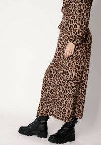 Długa sukienka w panterkę w odcieniach beżu i brązu, z długimi rękawami, zestawiona z czarnymi, skórzanymi botkami na sznurowadła z masywną podeszwą.