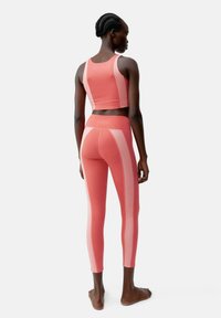Strak sportief crop top en leggings in het roze met contrasterende panelen. Soepele textuur, ronde achterkant en elastische tailleband.