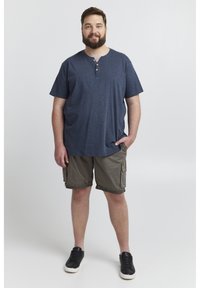 Blå kortærmet T-shirt med Henley-udskæring og tre knapper, parret med grå cargo shorts og sorte sneakers. Glat tekstur.