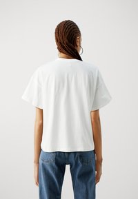 T-shirt en coton blanc avec des manches larges, un col rond et une coupe décontractée. Associé à un jean en denim bleu taille haute. Design simple et minimaliste.