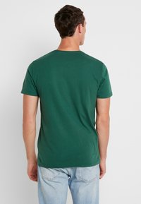 Grünes Baumwoll-T-Shirt mit kurzen Ärmeln, Rundhalsausschnitt und glatter Textur. Die Rückseite zeigt ein schlichtes Design ohne Logos oder Muster.