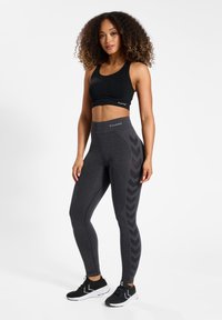 Czarny biustonosz sportowy i szare legginsy z wysokim stanem z wzorem zygzaka po boku, w zestawie z czarnymi butami sportowymi.