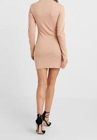 Robe ajustée à manches longues en ribbed de couleur beige clair, longueur genoux. Associée à des escarpins noirs à lanières. Texture lisse, design simple, sans motifs.