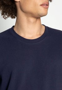 Granatowa koszulka typu crew-neck wykonana z teksturowanej bawełny, z ribbowanym dekoltem i gładkim materiałem. Zbliżenie na szczegóły tkaniny.