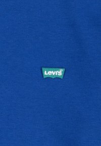 Camiseta de algodón azul con un pequeño parche del logo verde de Levi's en la parte delantera. La tela tiene un acabado suave y texturizado.